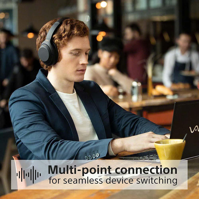 A man wearing the Sony wh-1000xm4 wireless noise-cancelling headphones switches easily between his mobile phone and laptop in a cafe