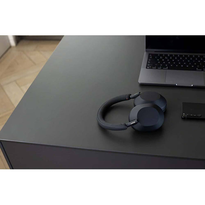 Sony WH-1000XM5 headphones and an Apple laptop sit on the desktop
